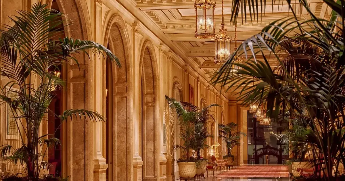 Lange hotelgang met marmeren vloer, palmen en kroonluchters in warm licht